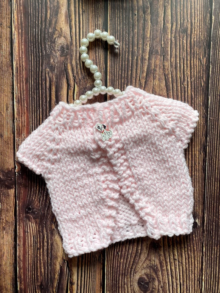 This top down chunky baby cardigan is knit in pink yarn and has a Dalmatian button sewn on