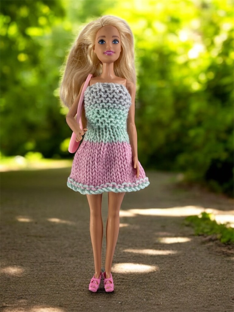 This is a barbie doll wearing a hand knit dress showing the design in the knitting pattern.