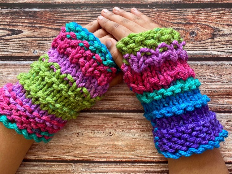 a pair of super chunky wrist warmer fingerless mittens worn on a pair of hands showing the mitts in the knitting pattern